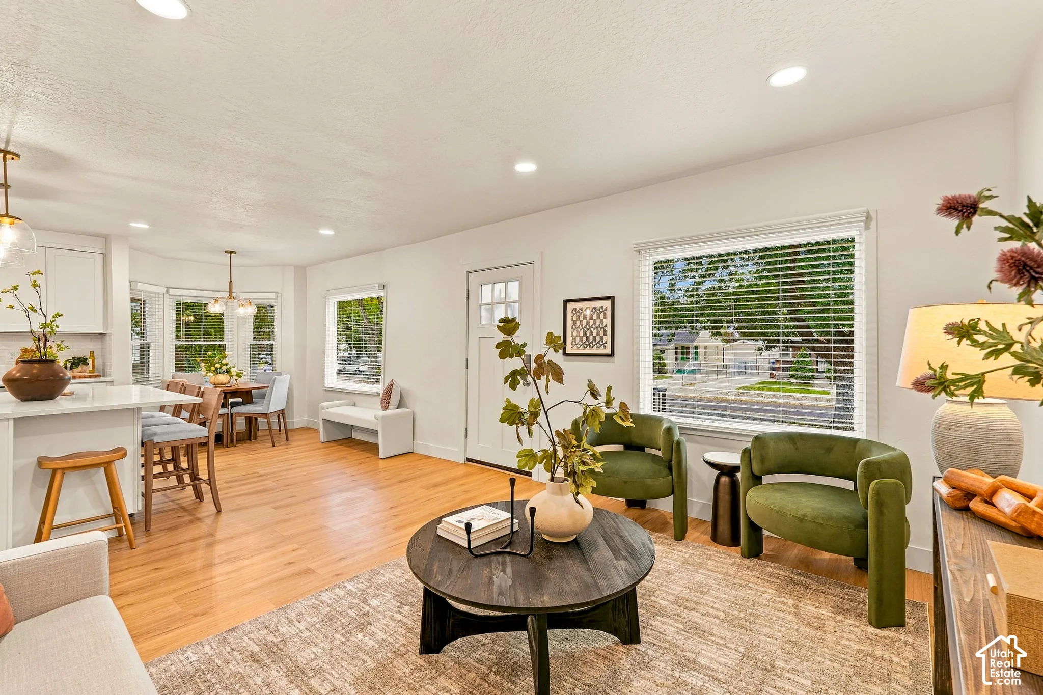 Hardwood flooring throughout, recessed lighting, white kitchen cabinetry, a kitchen island with seating, and a bay window in the dining area