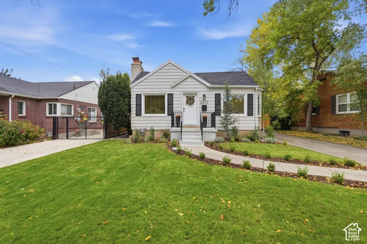 White siding exterior with black shutters, mature landscaping, paved driveway, wrought iron gate, and a concrete pathway leading to the entry