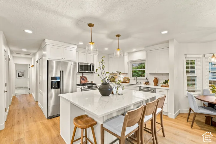 Kitchen featuring white shaker cabinetry, stainless steel appliances, a white island with seating, pendant lighting, and wood-finish flooring