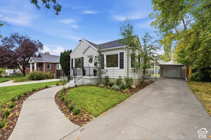 White siding exterior with black shutters, mature landscaping, concrete driveway, and covered carport with garage door