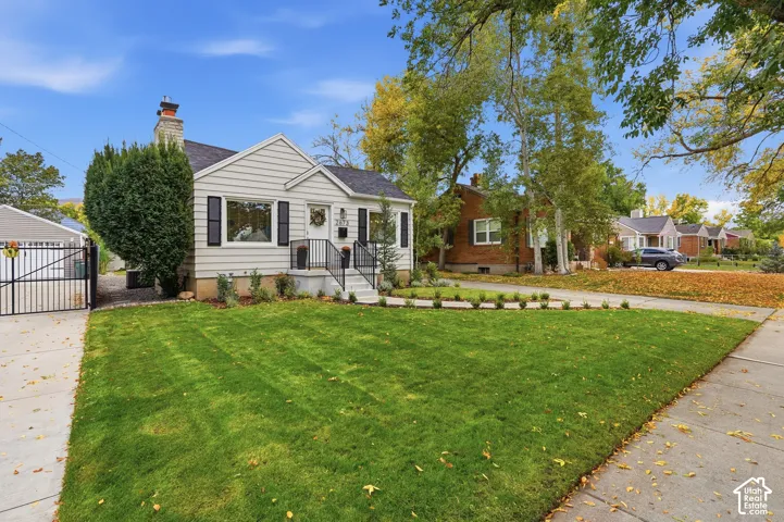 Siding exterior with black shutters, mature front lawn, concrete driveway, and wrought iron gate