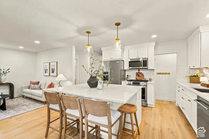 Open-concept living space featuring a white kitchen, center island with seating, stainless steel appliances, and wood-finish flooring