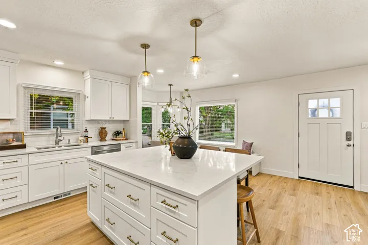 White cabinetry with brass hardware, a large kitchen island with a light-toned countertop, wood-finish flooring, and recessed lighting