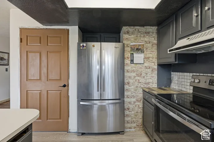 Kitchen area featuring dark cabinetry, stainless steel French-door refrigerator, electric range with matching overhead exhaust hood, and brick-pattern backsplash