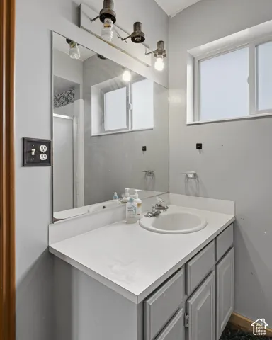 Bathroom vanity featuring a solid-surface countertop, integrated basin, cabinetry with panel detailing, large wall-mounted mirror, and industrial-style multi-light fixture