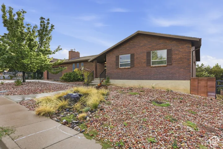 Brick exterior featuring an attached two-car garage, brick chimney, shuttered windows, and rock-covered landscaping