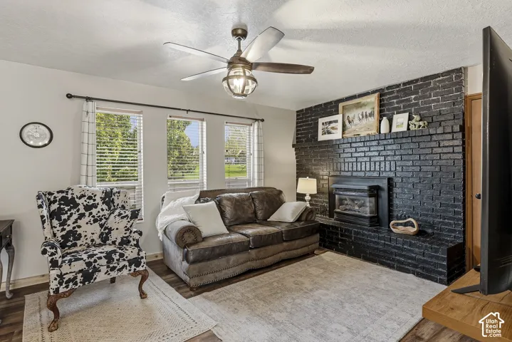 Floor-to-ceiling painted brick fireplace with a built-in insert, wood-finish flooring, and a multi-blade ceiling fan with integrated lighting