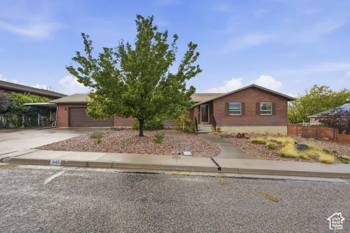 Single-level brick exterior featuring a multi-car garage, covered carport, concrete driveway, and xeriscaped front yard