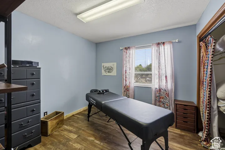 Room featuring wood-finish flooring, a central window with horizontal blinds, and a built-in closet with natural wood-tone trim