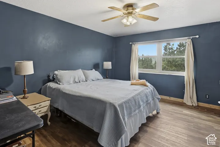 Bedroom featuring wood-finish flooring, a multi-blade ceiling fan with integrated lighting, and dual-pane window