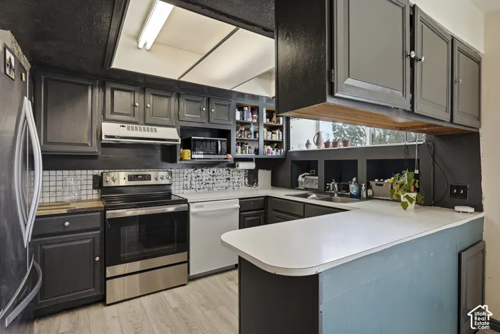 Kitchen featuring dark cabinetry, stainless steel range, built-in microwave, integrated light fixture, and wood-finish flooring