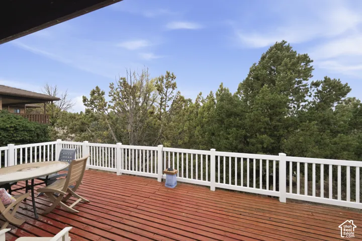 Elevated deck featuring wood-finish decking and a white balustrade railing, surrounded by mature coniferous trees
