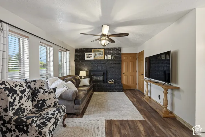 Living area featuring wood-finish flooring, a floor-to-ceiling painted brick fireplace, a built-in hearth, and a ceiling fan with integrated lighting
