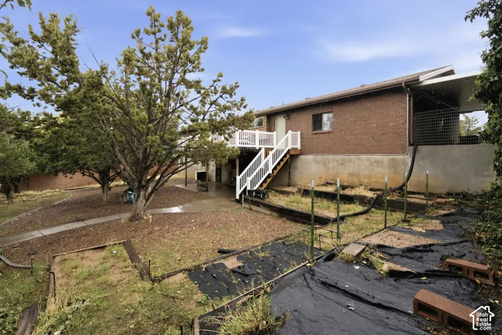 Brick exterior featuring an elevated wood deck with white railings, a covered parking structure, and terraced garden beds