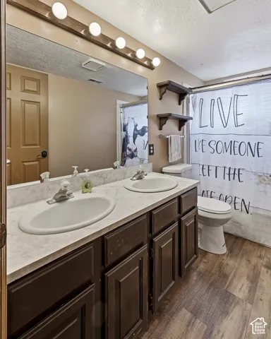 Dual-sink vanity with a solid surface countertop, wood-finish cabinetry, wall-mounted shelving, and wood-finish flooring