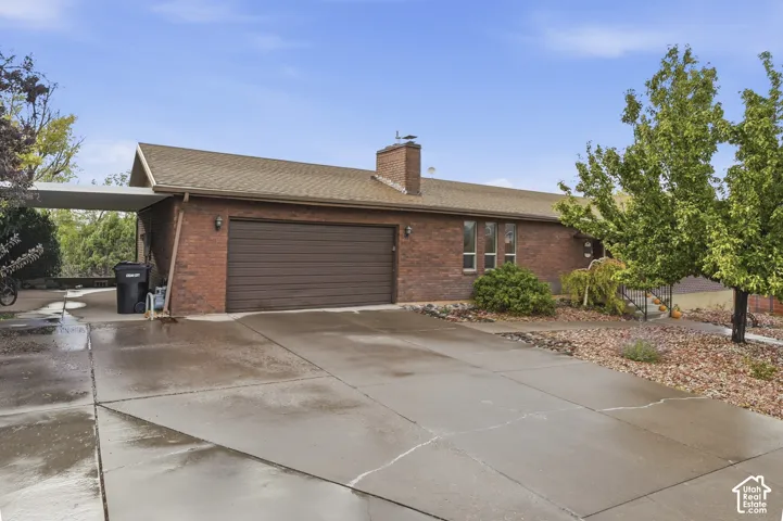 Brick exterior featuring a two-car garage, concrete driveway, attached carport, and masonry chimney