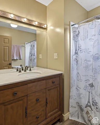 Vanity featuring dark wood cabinetry, a light-toned stone countertop with an integrated oval sink, and a full-width mirror with an attached linear light fixture