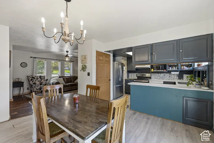 Kitchen featuring charcoal cabinetry, a breakfast bar, and stainless steel appliances, complemented by a dining area with a decorative candelabra chandelier and wood-finish flooring