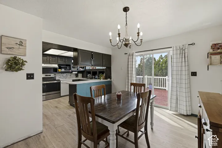 Kitchen featuring dark cabinetry, integrated stainless steel appliances, wood-finish flooring, a multi-arm chandelier, and a sliding glass door providing external access