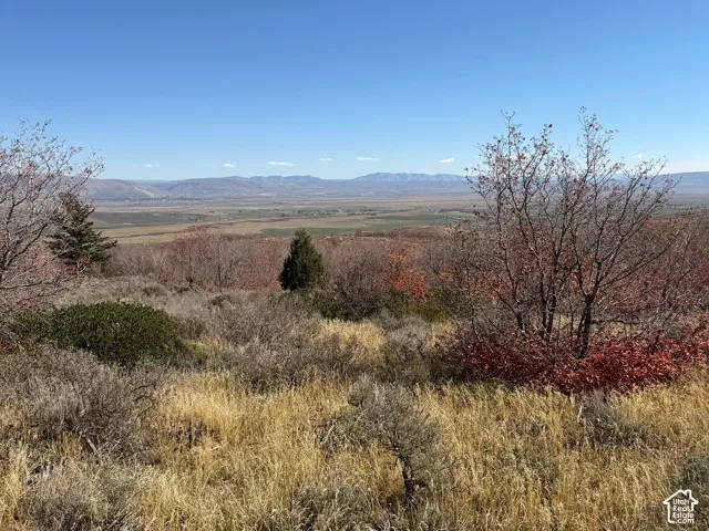 Expansive mountainous landscape with natural terrain, distant valley, and clear blue sky