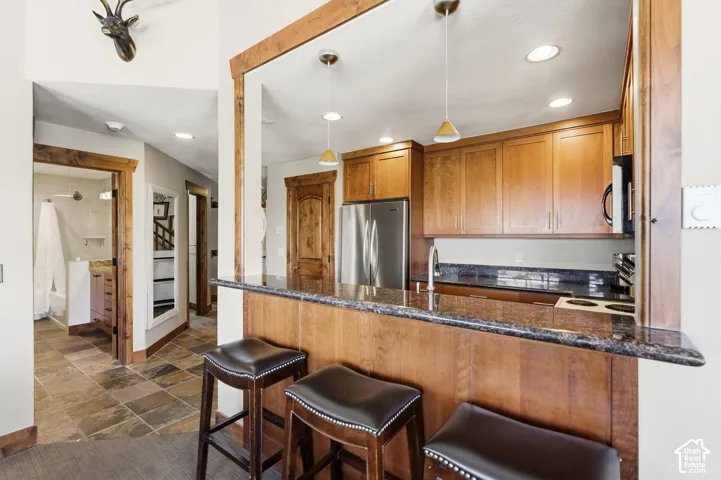 Kitchen featuring wood cabinetry, stone-surface breakfast bar, recessed lighting, and stainless steel appliances