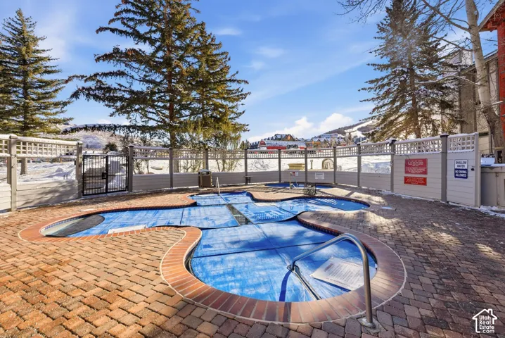 Outdoor pool area featuring brick paver decking, metallic handrails, and a perimeter privacy fence