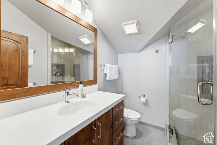 Bathroom featuring a wood-toned vanity with a solid-surface countertop, an integrated sink, a glass-enclosed shower with tiled surround, and a framed mirror