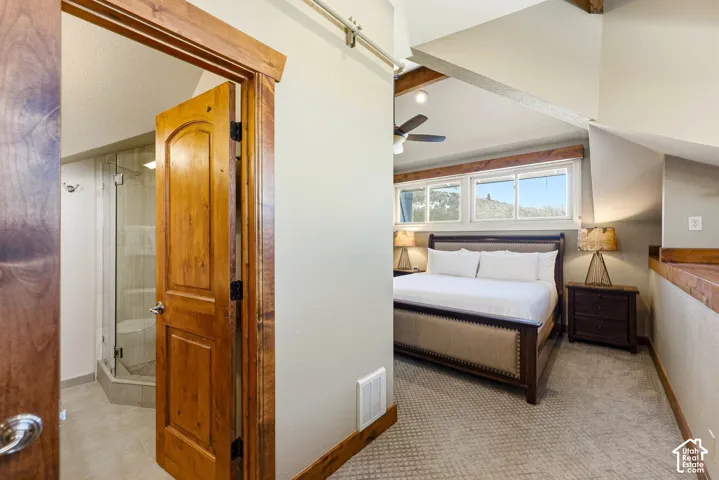 Vaulted ceilings with exposed wood beams, stained wood trim and doors, carpeted flooring, and a glass-enclosed shower with tile surround