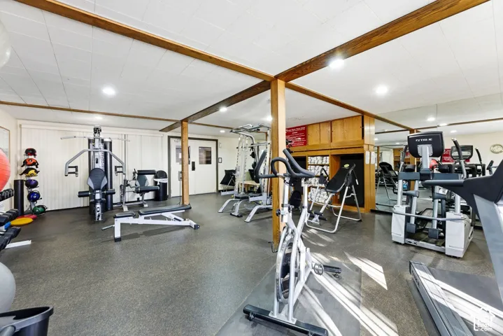 Expansive room featuring recessed lighting, mirror-paneled walls, built-in wooden cabinetry, durable rubber flooring, and exposed timber ceiling beams