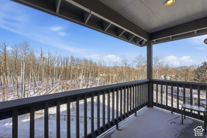 Covered balcony featuring dark-toned wooden railings, exposed rafter ceiling, recessed lighting, and a panoramic outlook of the surrounding forest