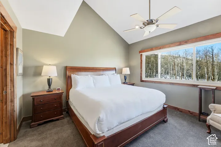 Vaulted ceiling featuring a central multi-blade ceiling fan, expansive horizontal window with natural wood trim, and carpeted flooring