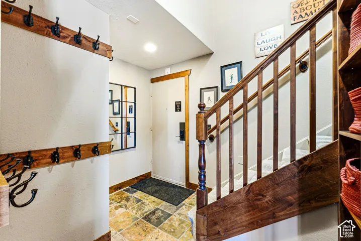 Entryway featuring multicolor natural stone tile flooring, a custom-built wood wall-mounted coat rack with matte black hardware, a wooden staircase railing with carved detailing, and recessed ceiling lighting
