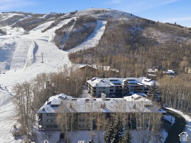 Snow-covered mountainous terrain featuring ski slopes, forested areas, and multi-story residential structures