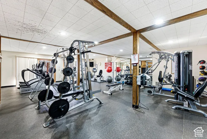 Fitness center with textured ceiling, exposed wood beams, resilient flooring, and multiple exercise machines