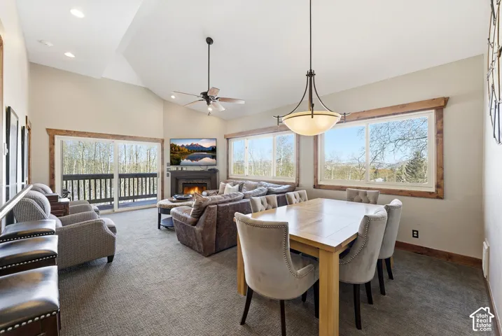 Vaulted ceilings, a stone-surround fireplace, wooden window trim, a ceiling fan, and sliding glass doors with exterior balcony access
