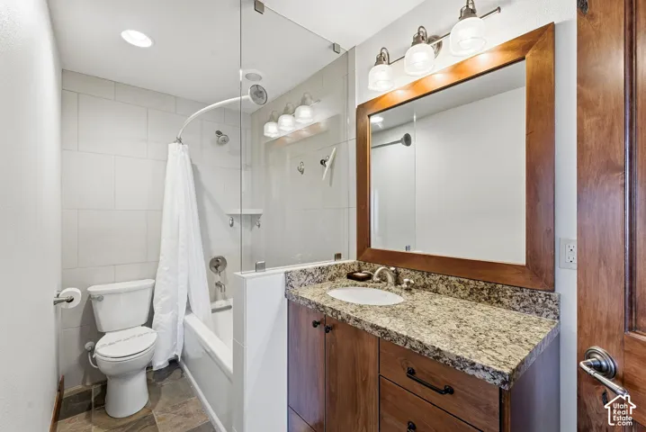 Bathroom featuring a wood-finish vanity with a granite-style countertop, undermount sink, and a framed mirror