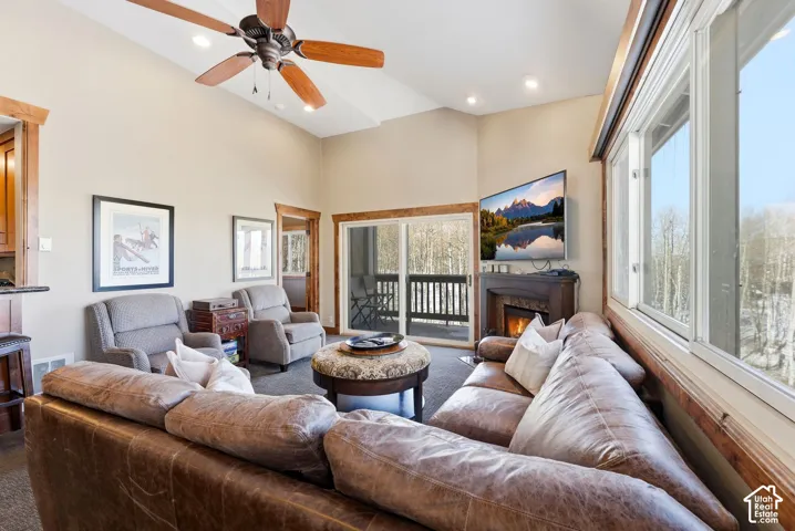 Vaulted ceilings, floor-to-ceiling windows, wood-trimmed door and window casings, a fireplace with a mantel, and a sliding glass door