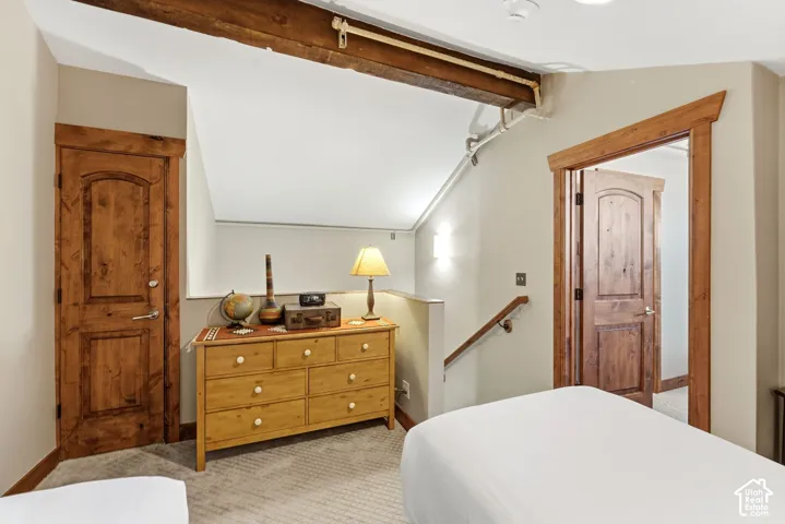 Sloped ceiling room featuring warm wood doors, exposed ceiling beams, and a carpeted floor