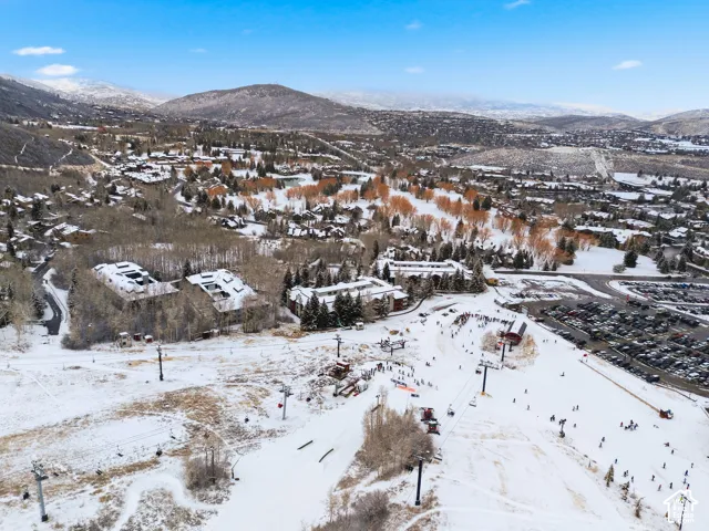 Snow-covered mountain landscape with ski slopes, multiple ski lifts, and a complex of buildings featuring pitched roofs and a large parking area