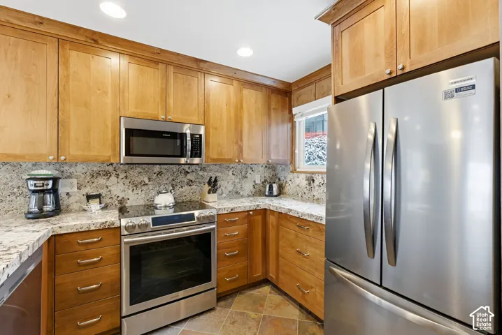 Kitchen featuring stainless steel appliances, light wood cabinetry, granite countertops, and a stone tile floor