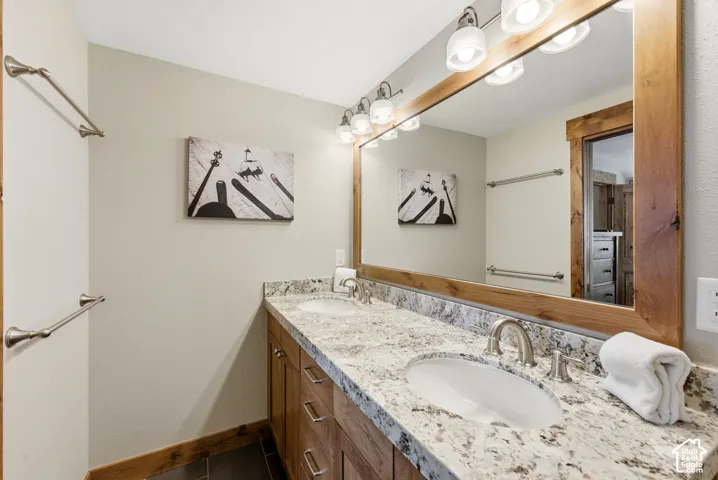 Double vanity with undermount sinks, stone countertop, wood-finish cabinetry, and framed mirror with integrated lighting