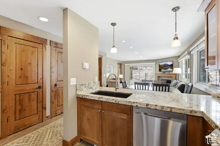 Kitchen featuring stone countertops, integrated sink, stainless steel dishwasher, and pendant lighting