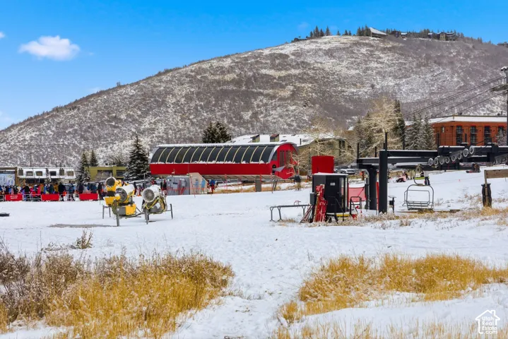 Snow-covered landscape featuring a ski lift structure, a gondola station, and distant buildings