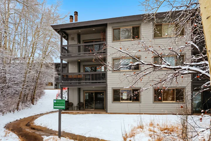 Multi-level building with light gray siding, dark trim, multiple balconies, and a patio space