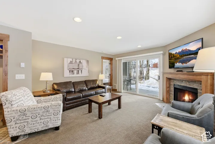 Carpeted living area featuring a stone-surround fireplace with a wood mantle, recessed lighting, and a sliding glass door to the exterior