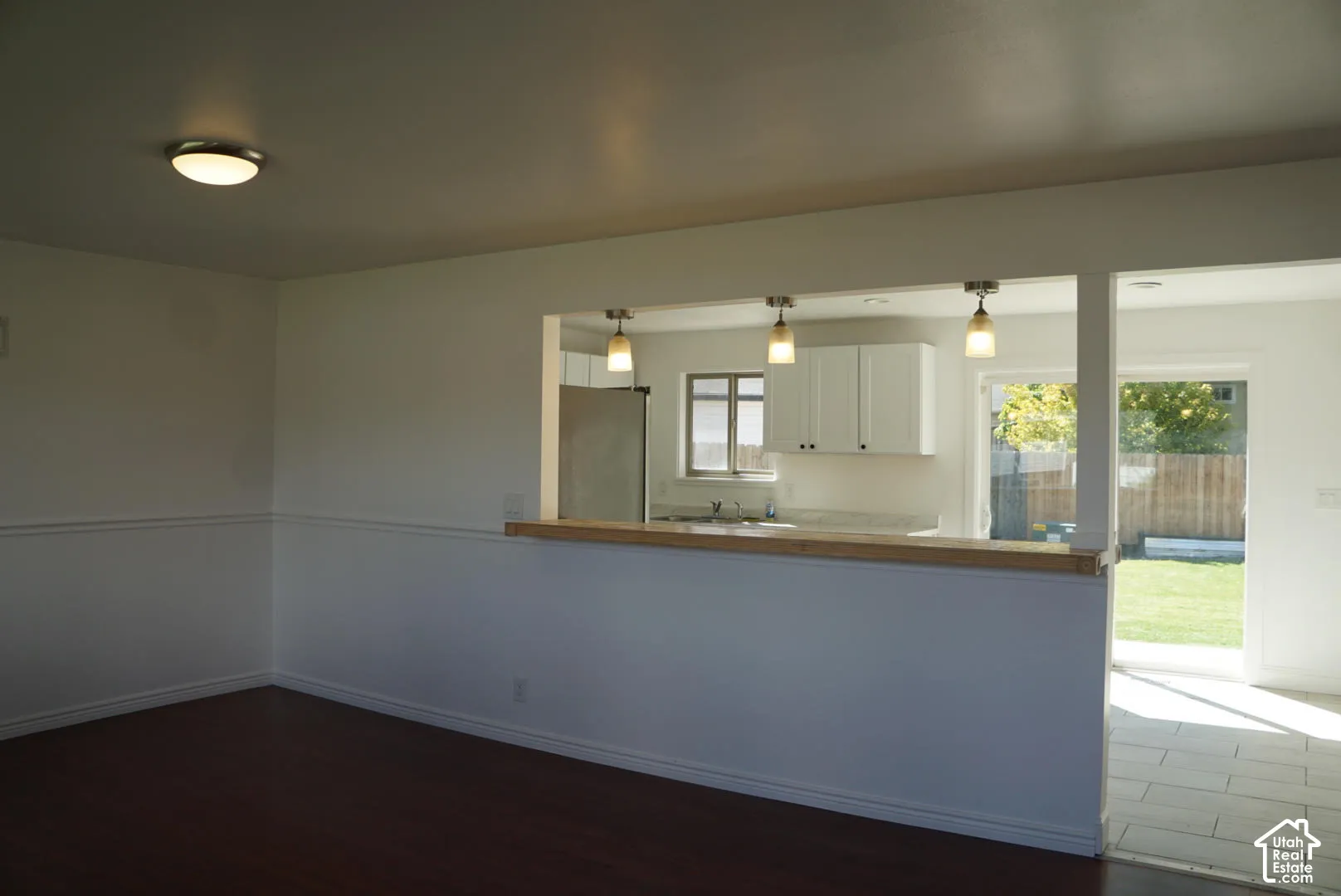 Pass-through wall opening with a wood-finish bar top, three pendant lights, white cabinetry, and sliding glass doors