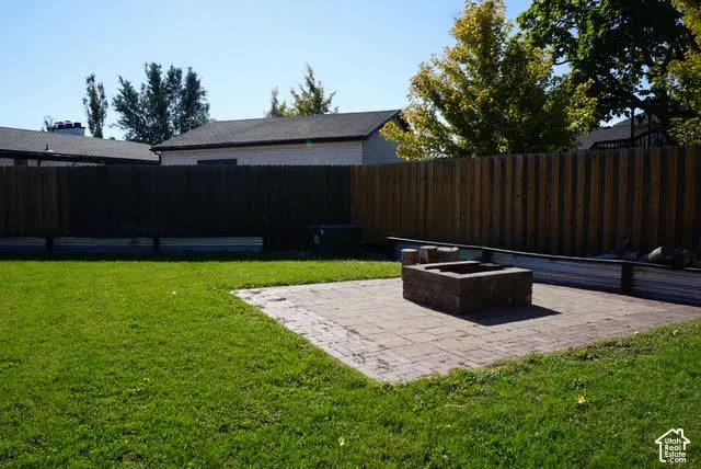 Backyard featuring a manicured lawn, a paved patio, a built-in masonry fire pit, and a full-height wood privacy fence