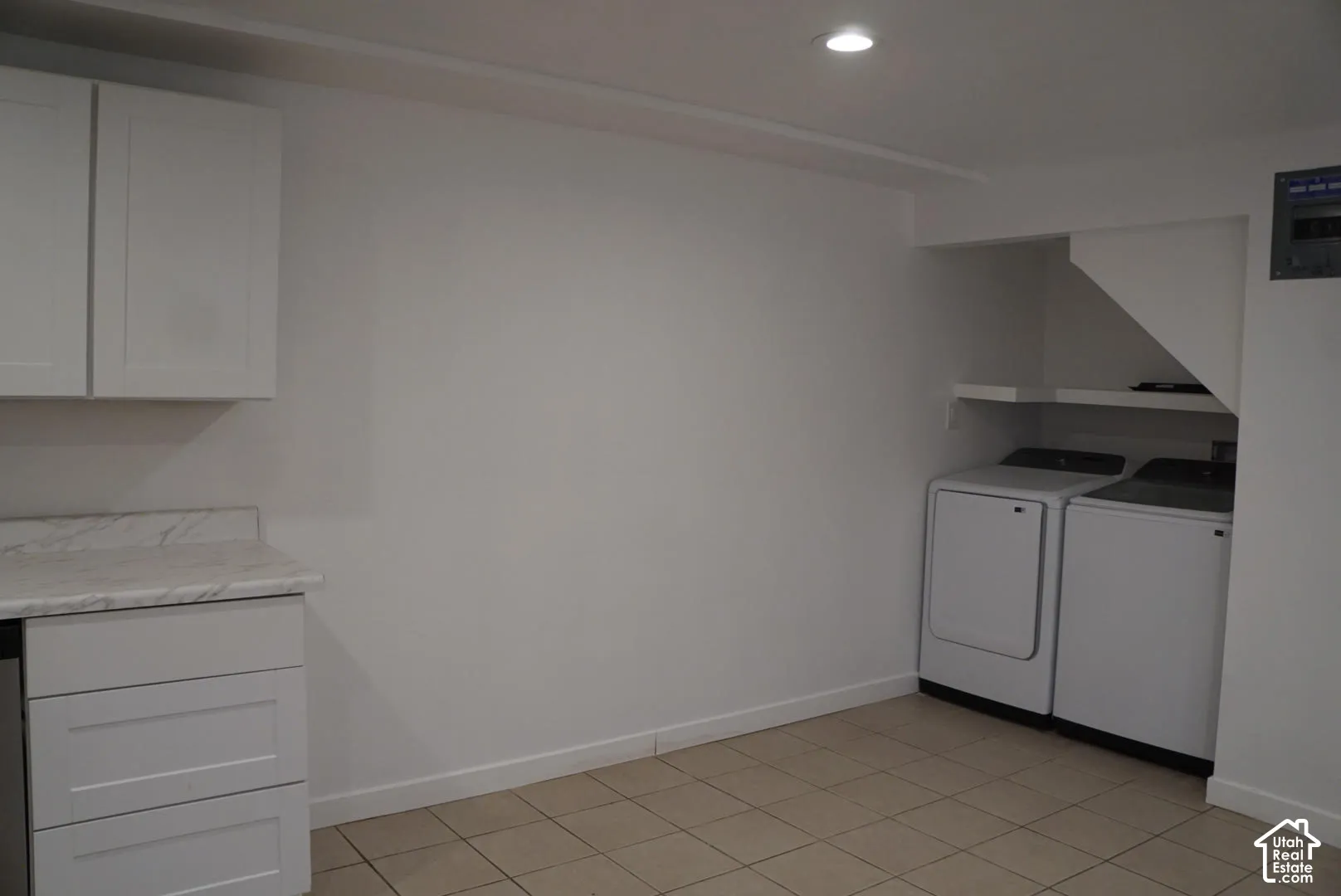 Laundry area featuring white shaker-style cabinetry, stone-patterned laminate countertop, neutral tile flooring, and recessed ceiling lighting