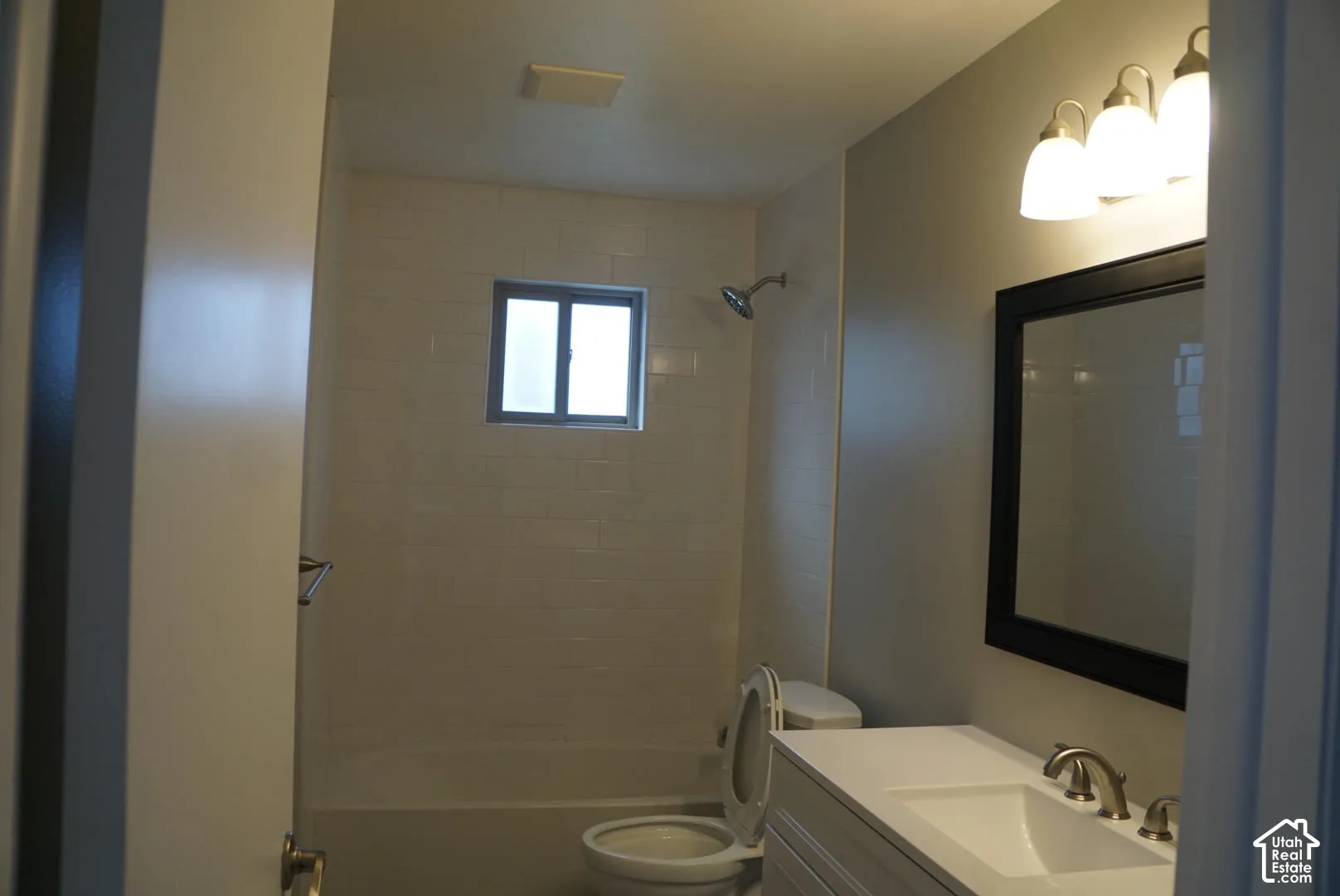 Bathroom featuring a white vanity with an integrated basin, a three-light vanity fixture, a framed wall mirror, and a tub-shower combination with tiled surround
