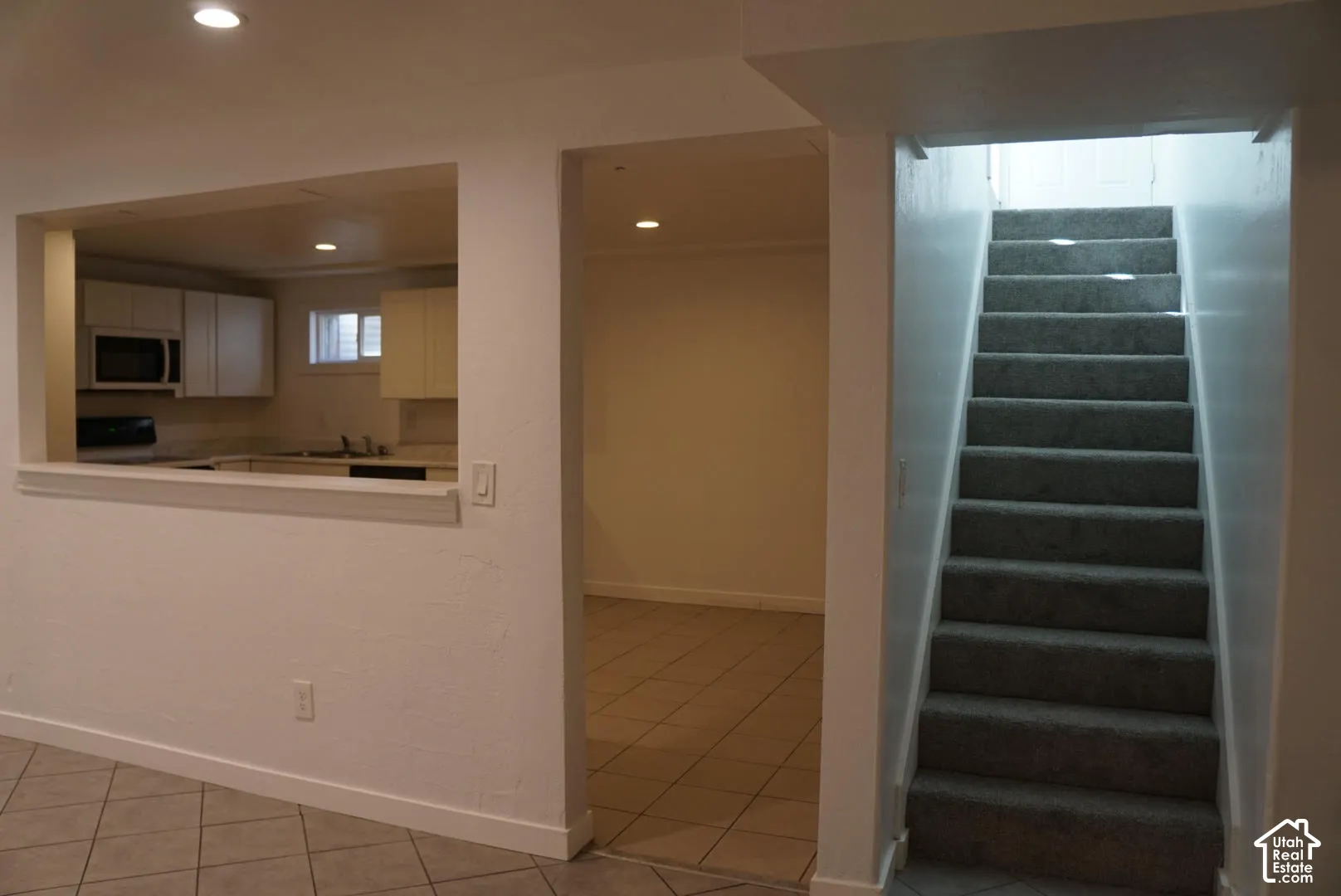 Kitchen featuring flat-panel cabinetry and built-in appliances, accented by a pass-through opening, ceramic tile flooring, and a carpeted staircase